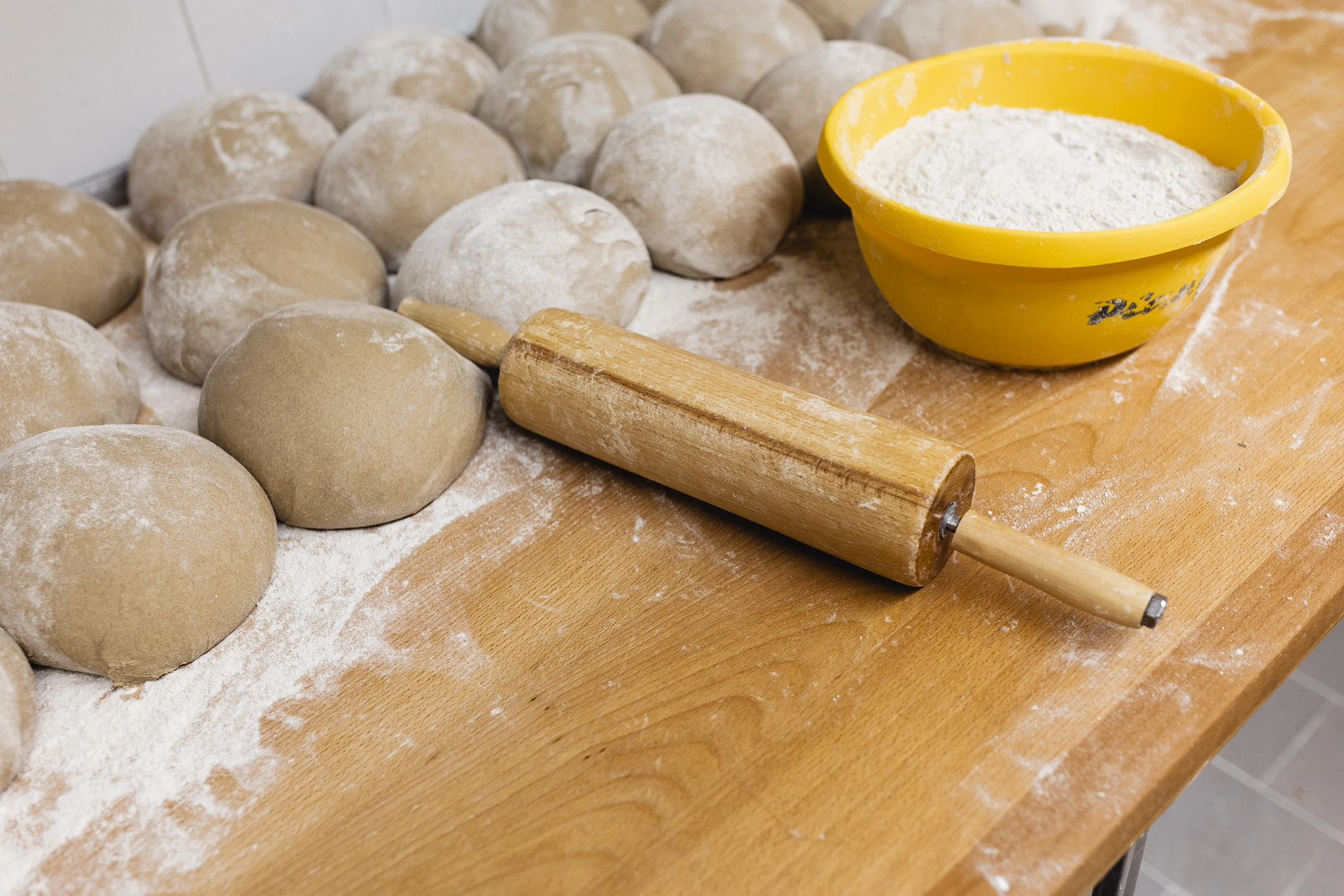 Frisch und sorgfältig geformte Brötchen aus Teig auf einer bemehlten Arbeitsfläche mit danebenliegendem Nudelholz.