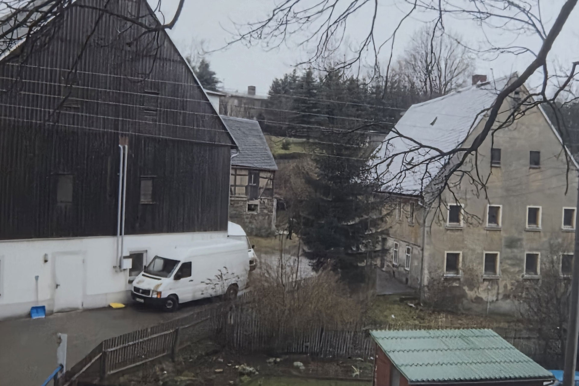 Aufnahme der Scheune mit dunkler Holzfassade und des angrenzenden Gebäudes auf einem Hofgelände.