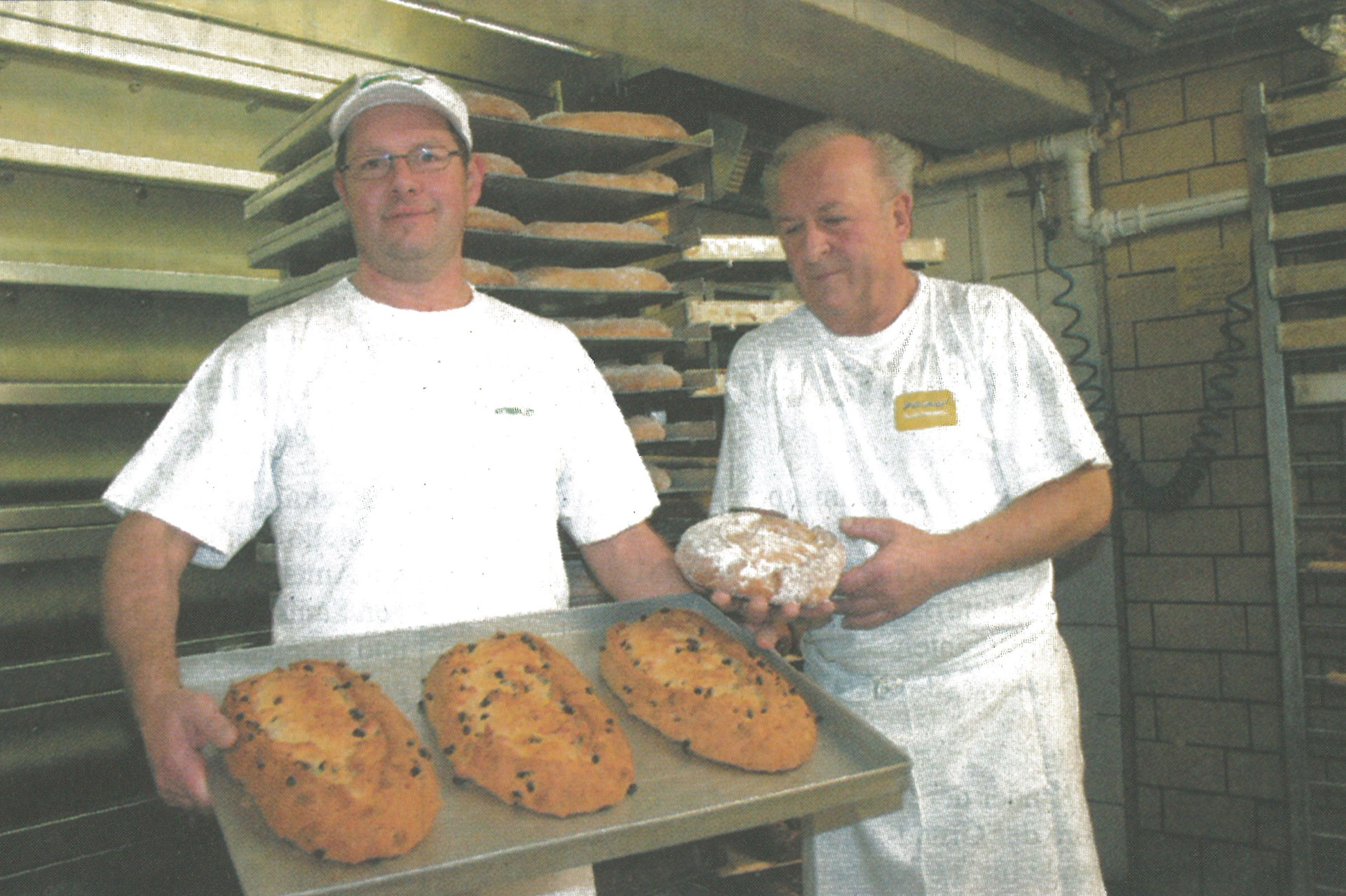 Mathias Göpfert und der Altmeister präsentieren frisch gebackenes Brot auf einem Blech in der Backstube.